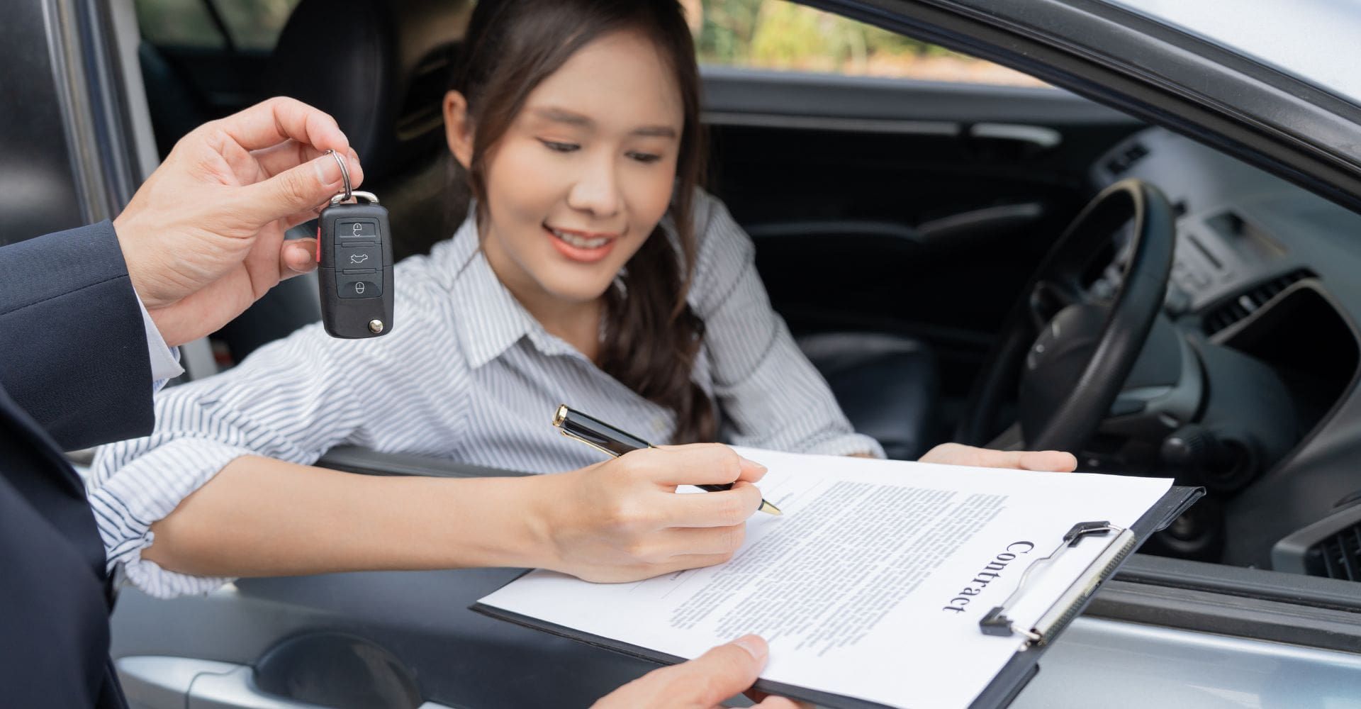 woman signing paperwork as she's being handed the keys to a rental car