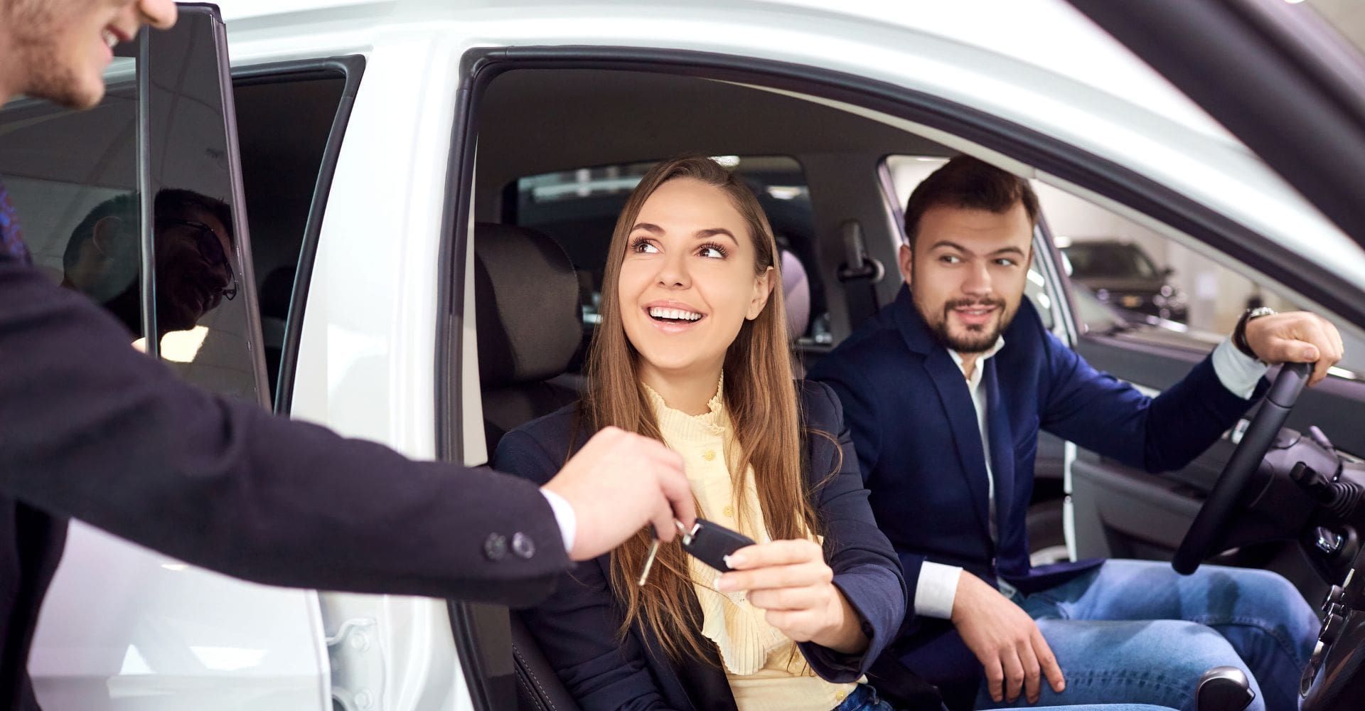 couple sitting in a rental car being handed the keys 