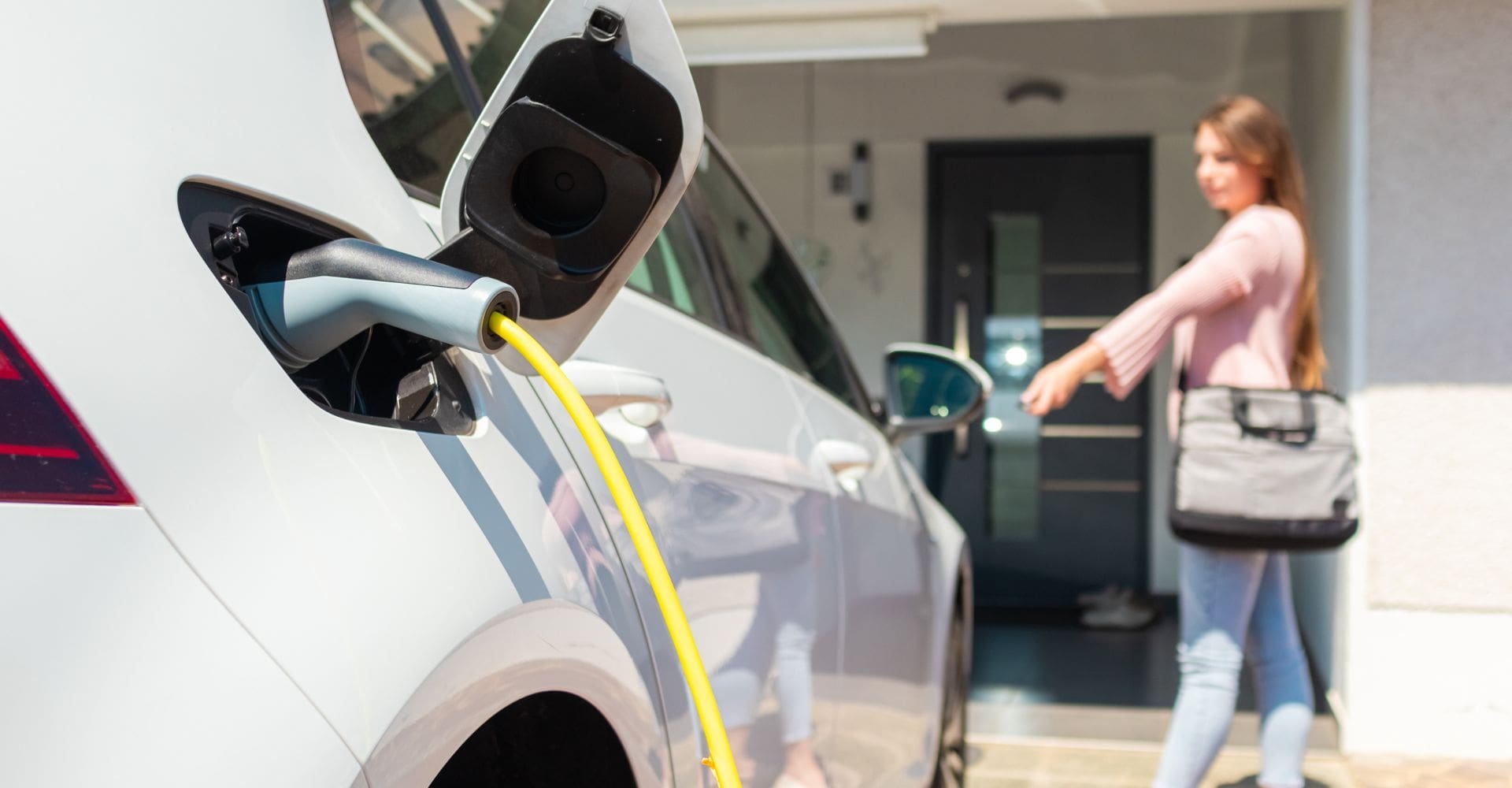 woman walking away from an electric car after plugging in the charger 