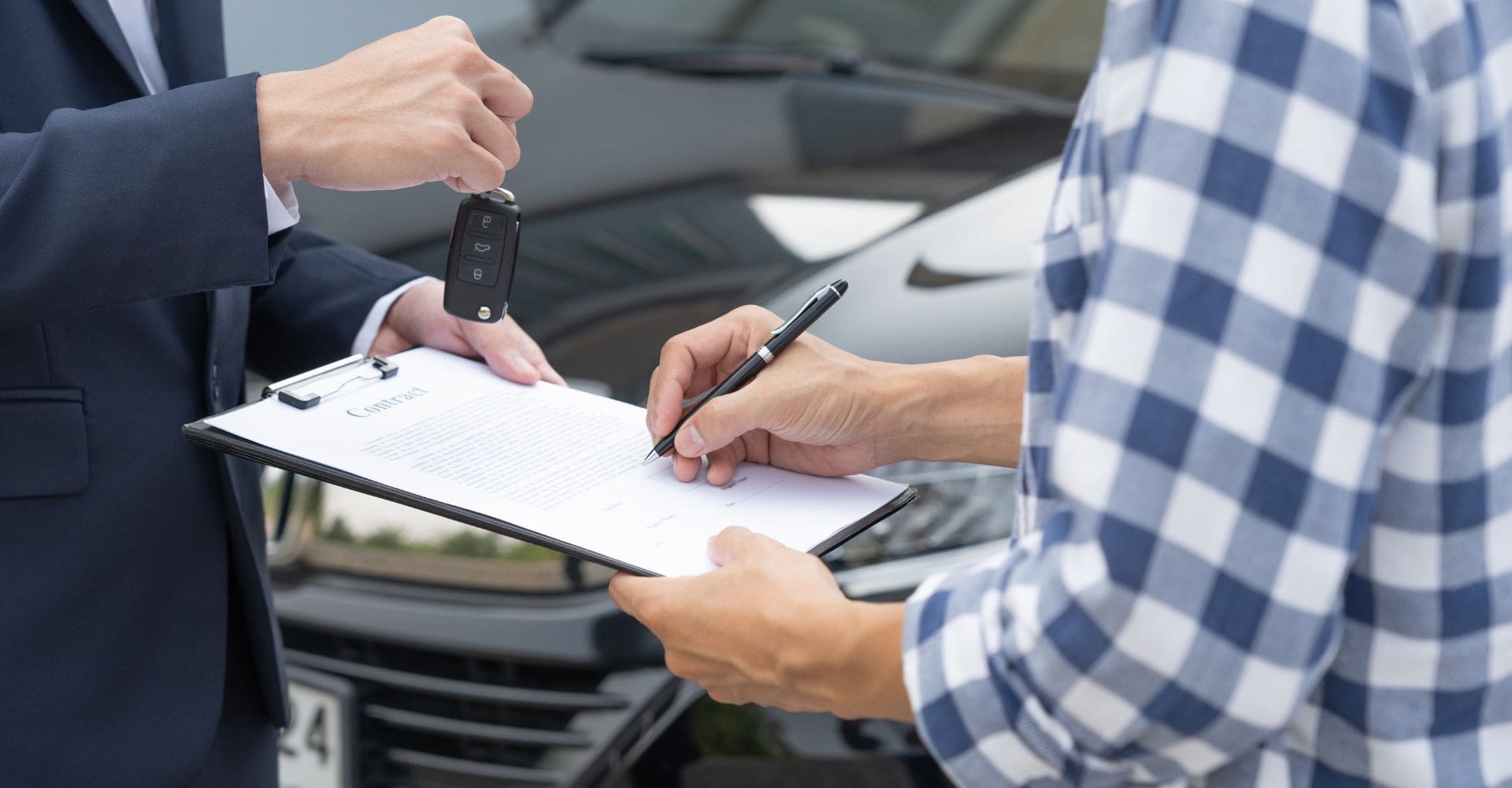 person in a plaid shirt signing a rental car agreement and being handed car keys