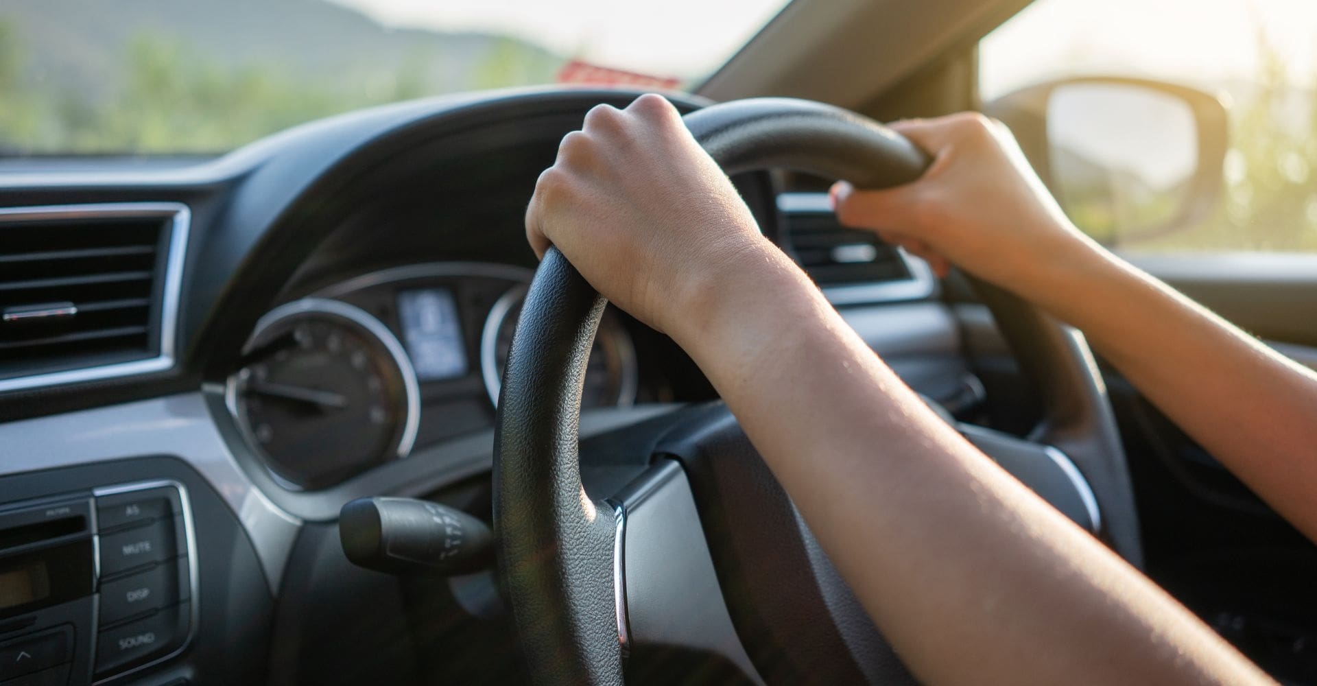 interior view of someone driving a car with two hands on a steering wheel 