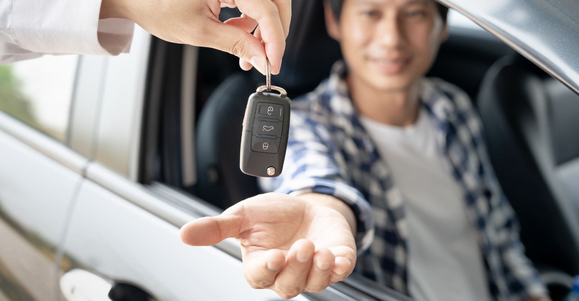 person sitting in a car with their hand outstretched receiving keys to a rental car