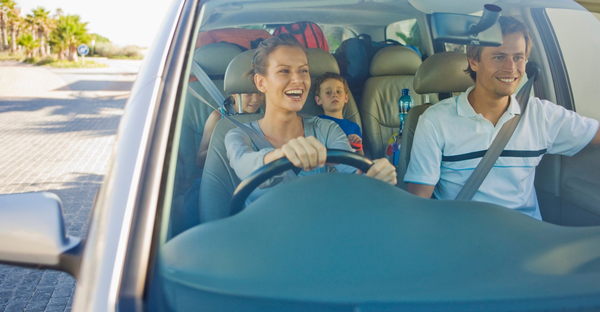 a family smiling in their rental car while driving down the road