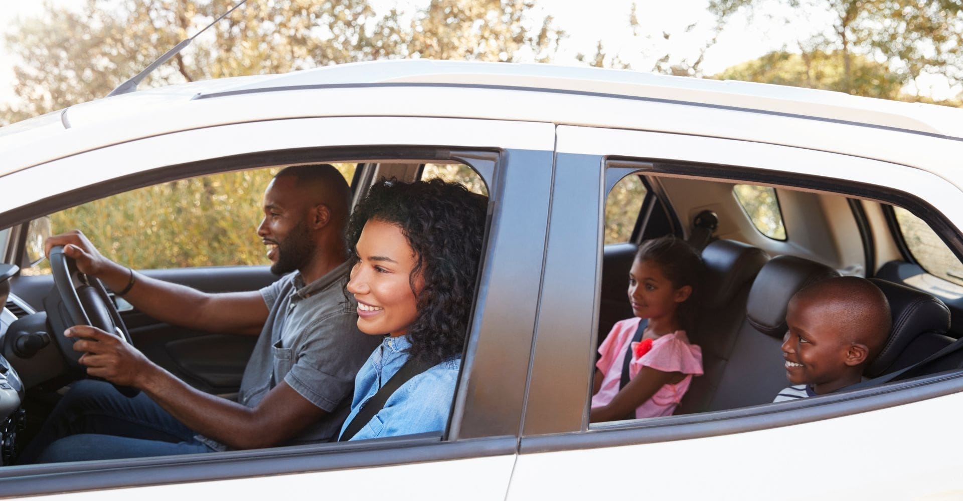 parents in front and kids in the back of a sedan looking excited about their trip 