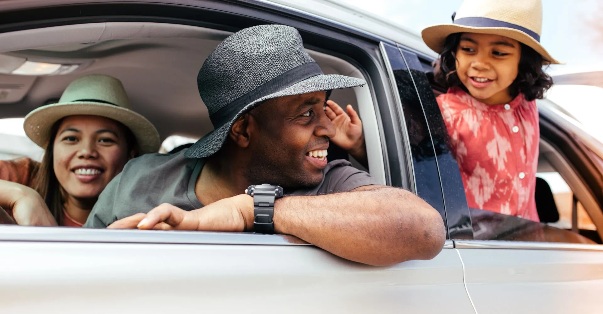 a couple and their child hanging out of the windows of their rental car getting ready to take a road trip 