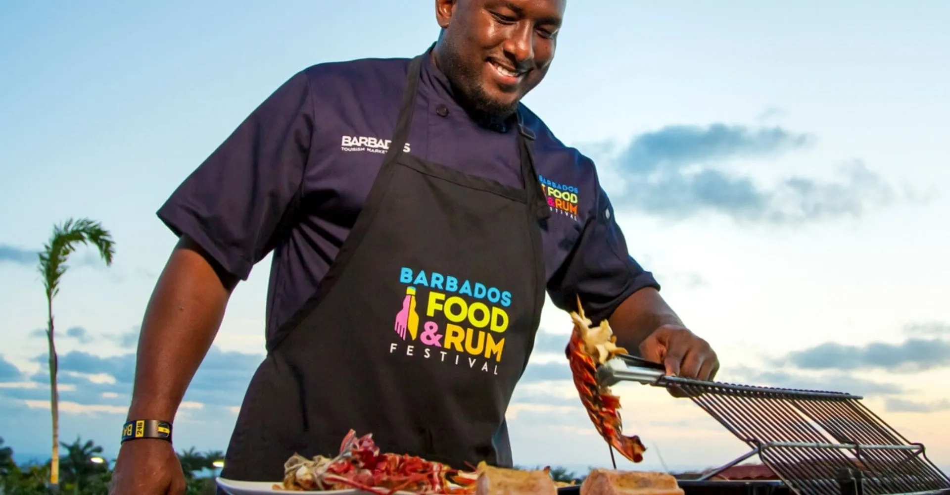 A man wearing an apron grills food on a barbecue, surrounded by outdoor greenery