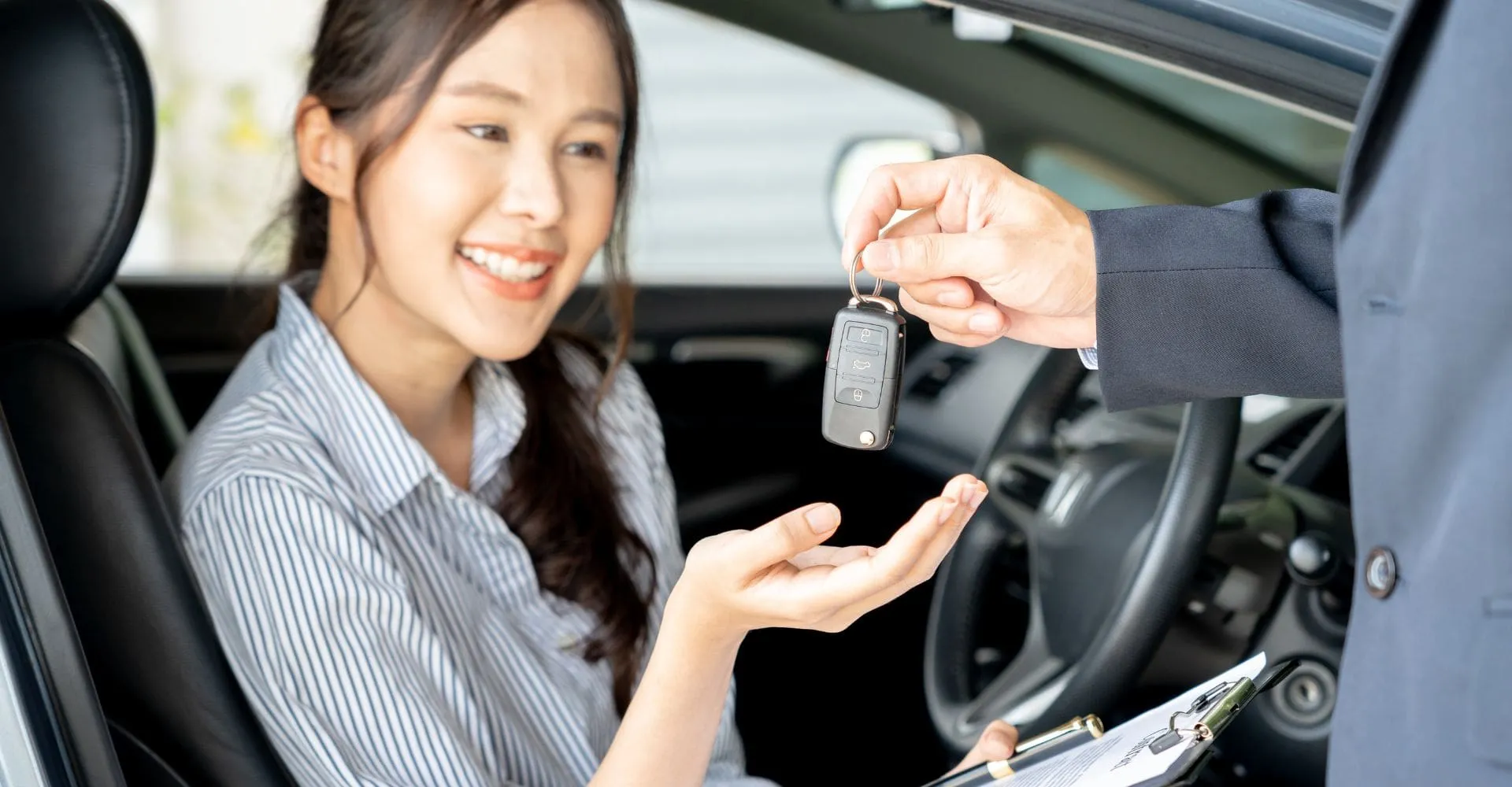A woman smiles while holding a car key, expressing joy and excitement about her vehicle
