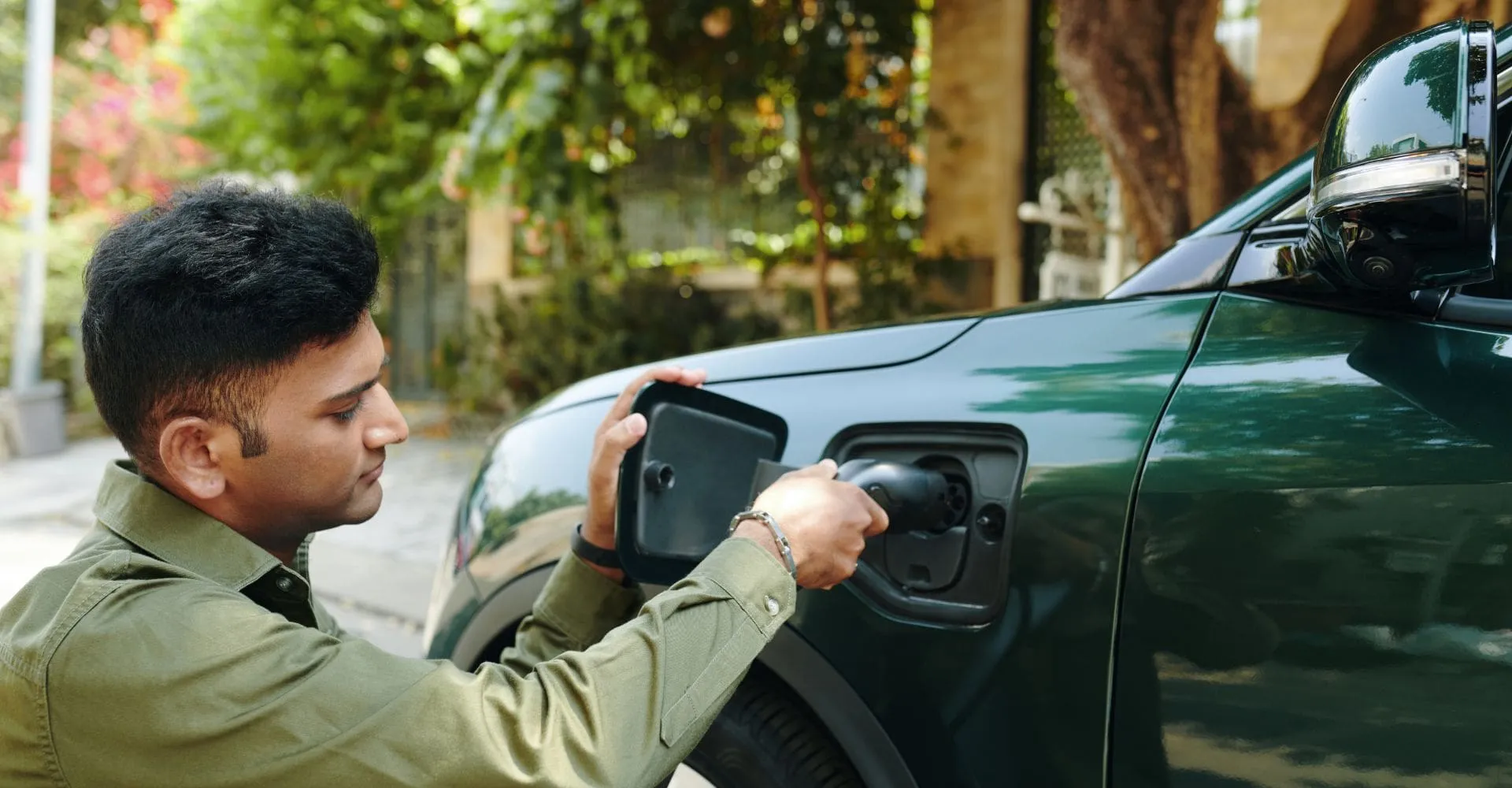 A man plugging in a green electric car preparing to charge it