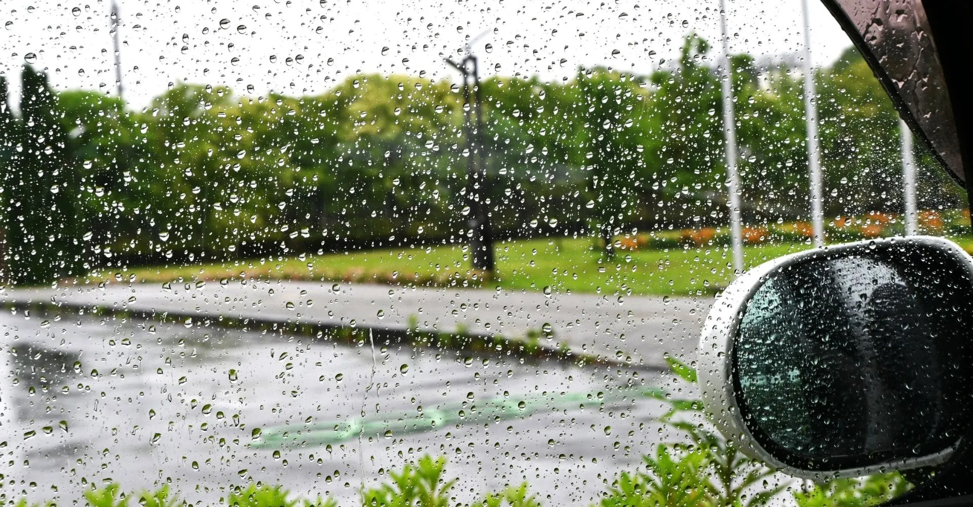 A close-up view of a car window covered in raindrops, blurring the outside scenery