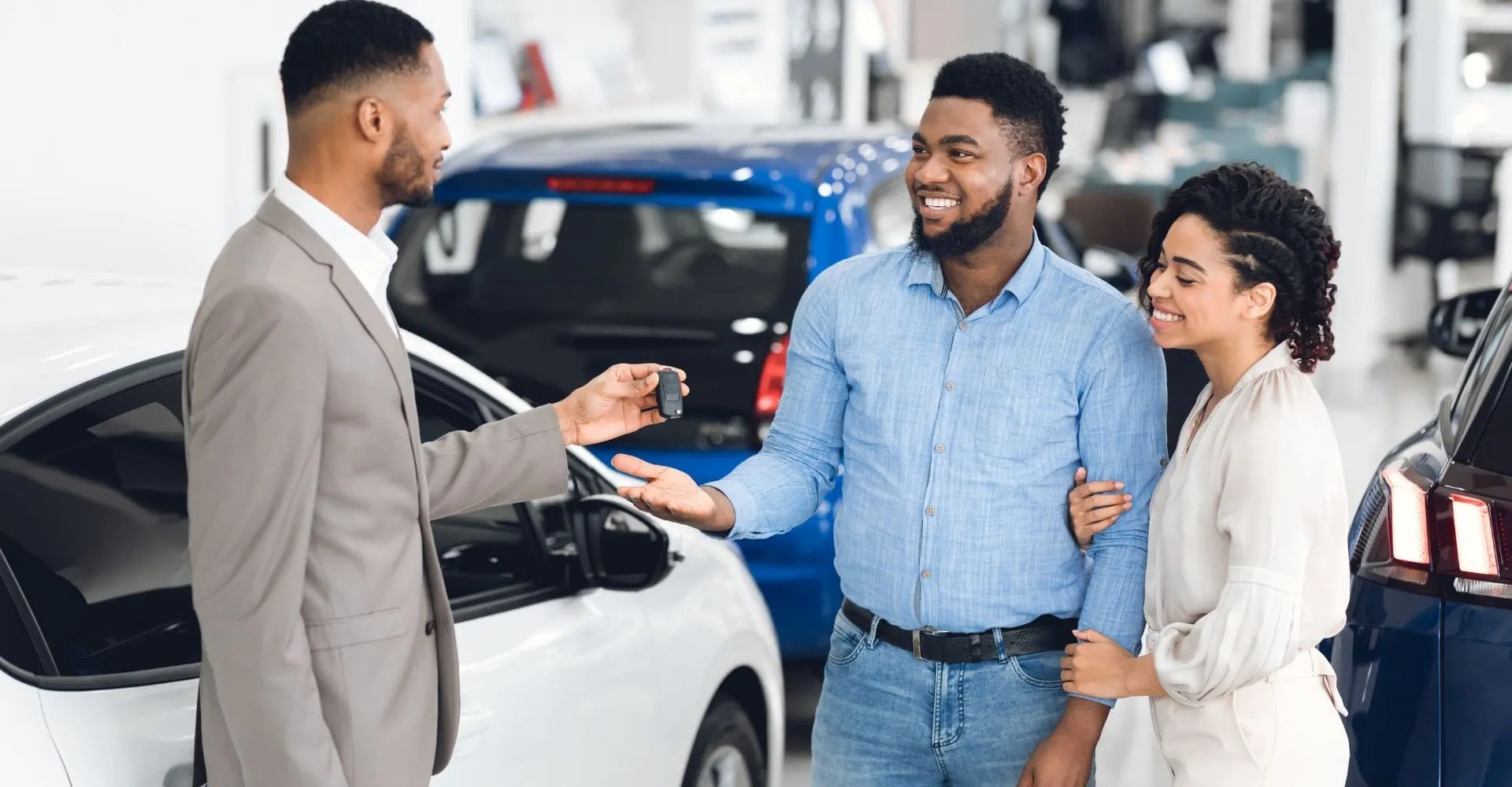 A man and woman stand together in front of a parked car, smiling and engaged in conversation