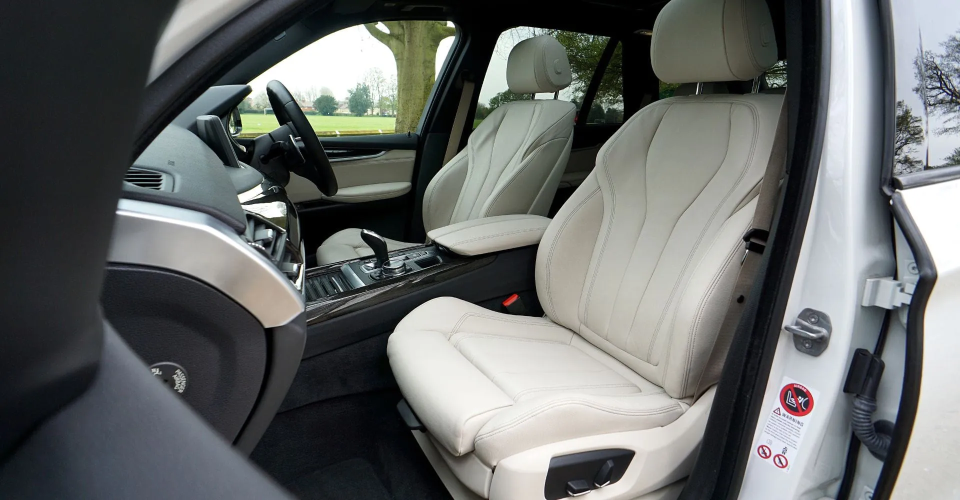 The interior of a luxury car, featuring plush white leather seats and a sleek design. The surrounding landscape is visible through the windows.
