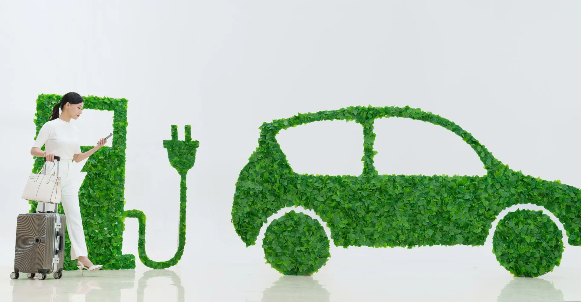 A woman in white with luggage stands beside a green, leafy electric car and charging station silhouette, symbolizing eco-friendly travel.