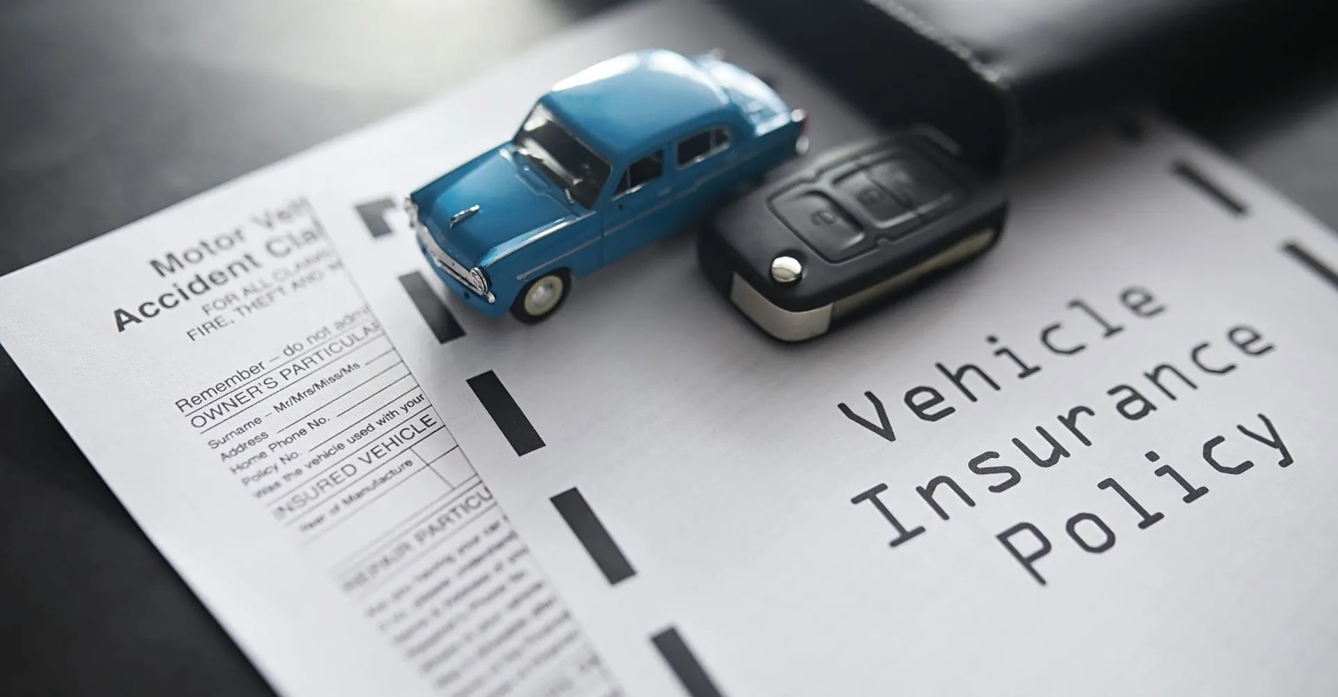 A toy blue car and a black car key rest on a vehicle insurance policy document, symbolizing auto coverage and protection.v
