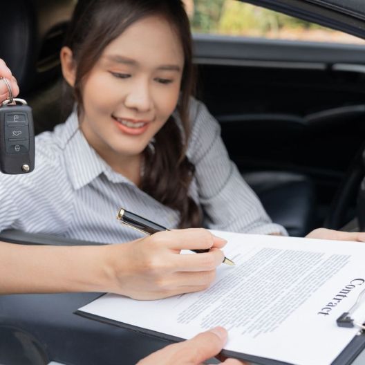 woman signing paperwork as she's being handed the keys to a rental car
