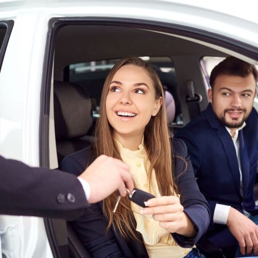couple sitting in a rental car being handed the keys 