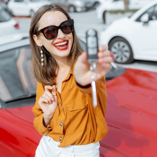 woman wearing sunglasses holding up the keys to her red rental car in excitement 