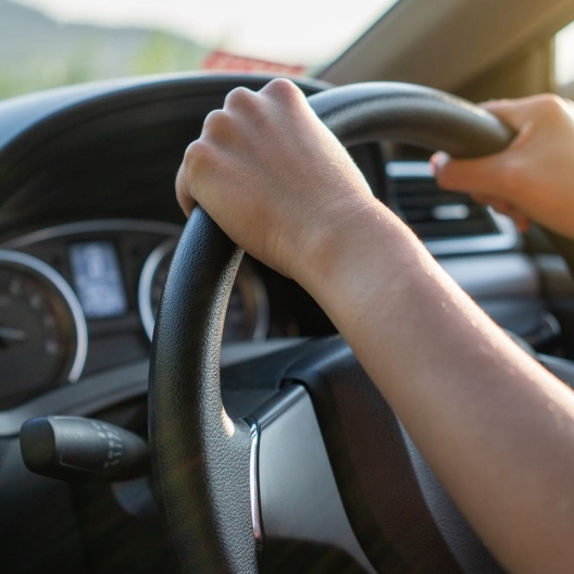 interior view of someone driving a car with two hands on a steering wheel 