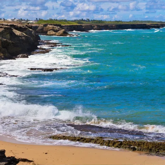 a man wearing a sun hat and protective layers taking pictures on the coast on a windy day in Barbados