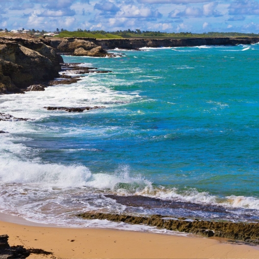 a man wearing a sun hat and protective layers taking pictures on the coast on a windy day in Barbados