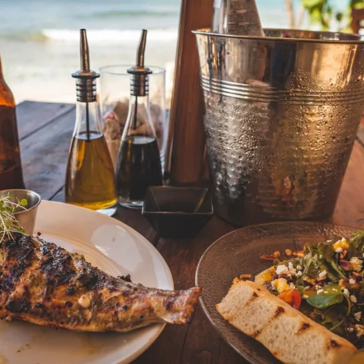two plates of Bajan food on a table overlooking the ocean 