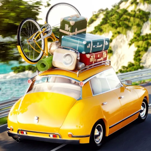 A yellow car with luggage on its roof driving along a scenic road under a clear blue sky