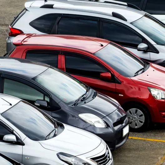 A row of various cars parked in a spacious parking lot under clear blue skies