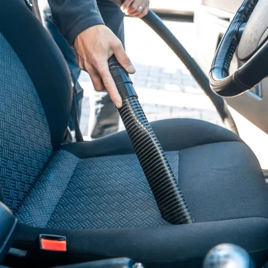 A person using a vacuum to clean the interior of a car, focusing on the seats and floor mats
